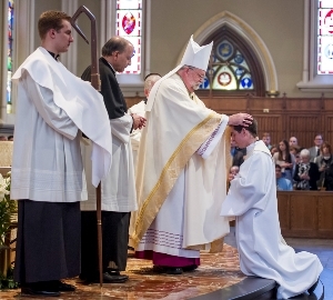 Bishop Jenky lays hands on Chase Pepper, CSC, during Ordinations