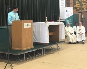 Colby McLiverty '16 addresses his fellow students at the end of Moreau Day Eucharistic Liturgy at Notre Dame High School, with seated to the right, Father Joseph A